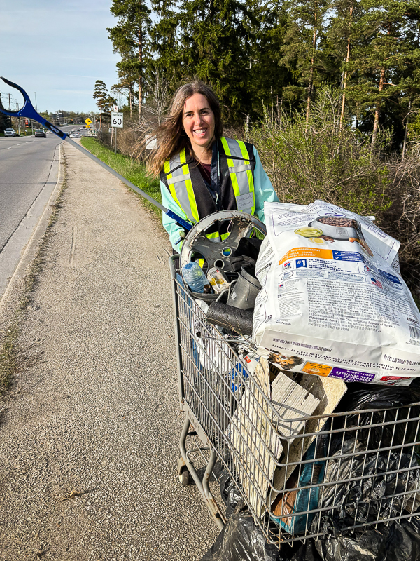 A volunteer in a high-visibility vest pushing a shopping cart loaded with collected litter during a cleanup