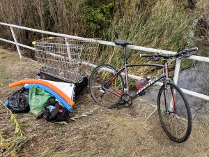 A bike trailer getting loaded with a shopping cart, pool noodles and other debris recovered during a cleanup