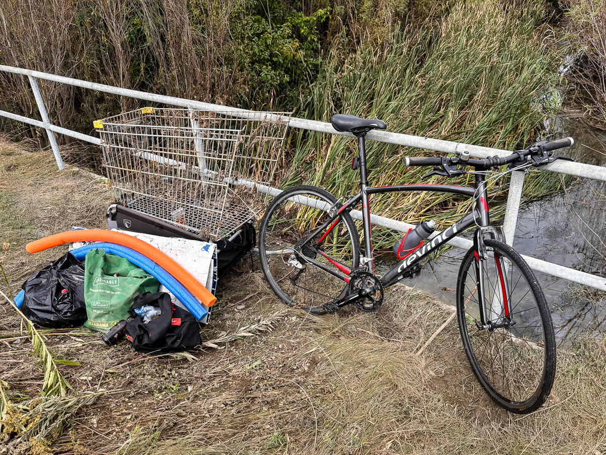 A bike trailer getting loaded with a shopping cart, pool noodles and other debris recovered during a cleanup